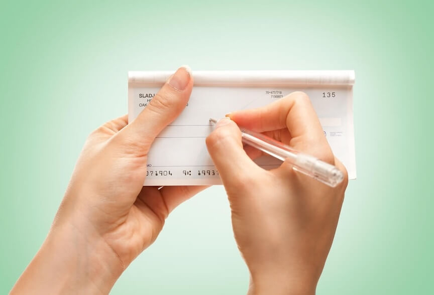 A person writing a check with their own name on the Pay to the order of line