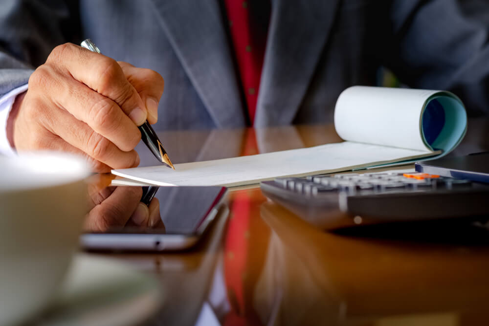 Business Man in Grey Suit Signing Blank Check Book