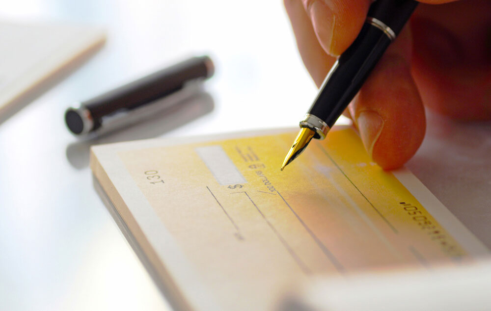 Person signing a check with pen representing mailing checks safely during the pandemic.