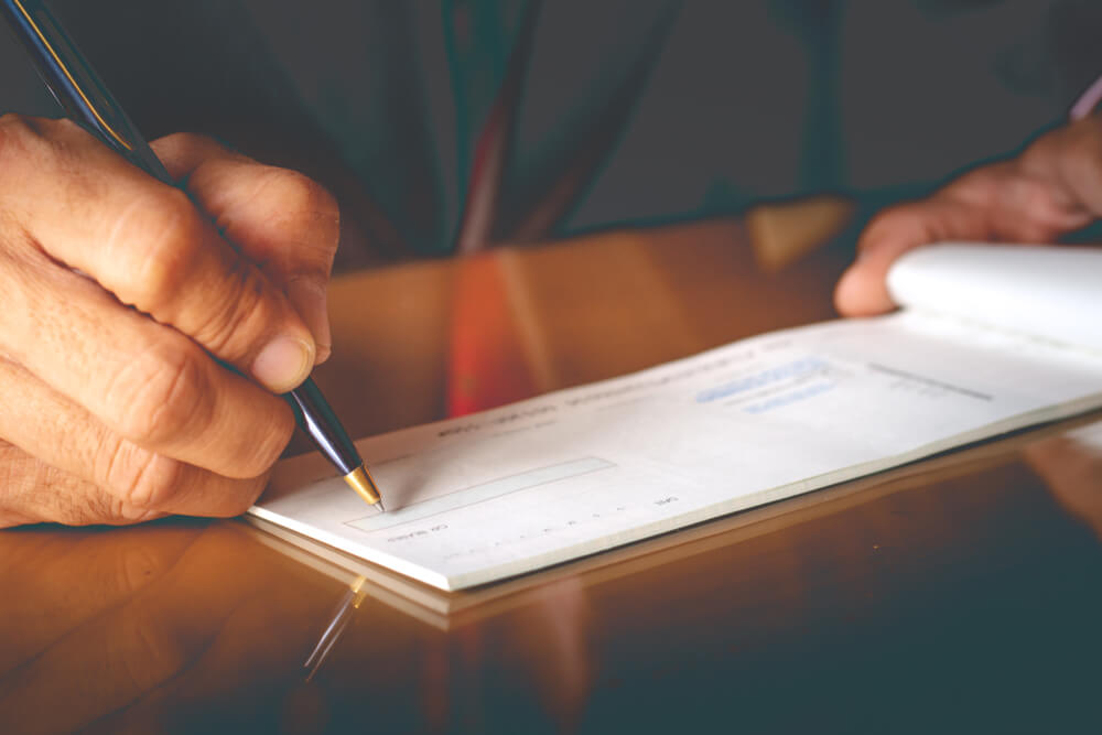 Closeup of Businessman Hand Writing and Signing Check on the Table at Office