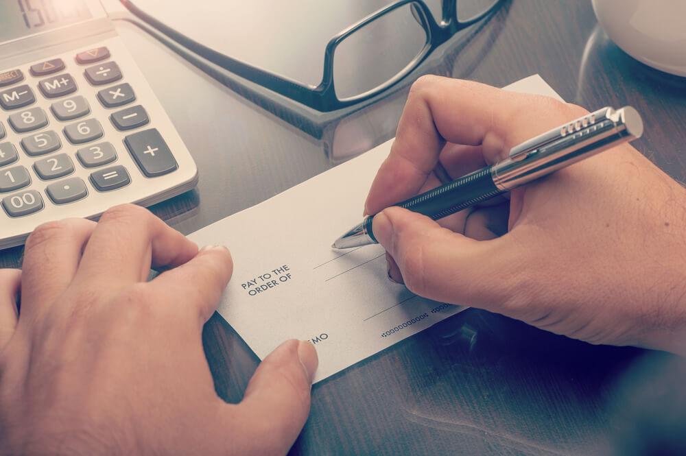 Man Writing a Payment Check at the Table With Calculator and Glasses