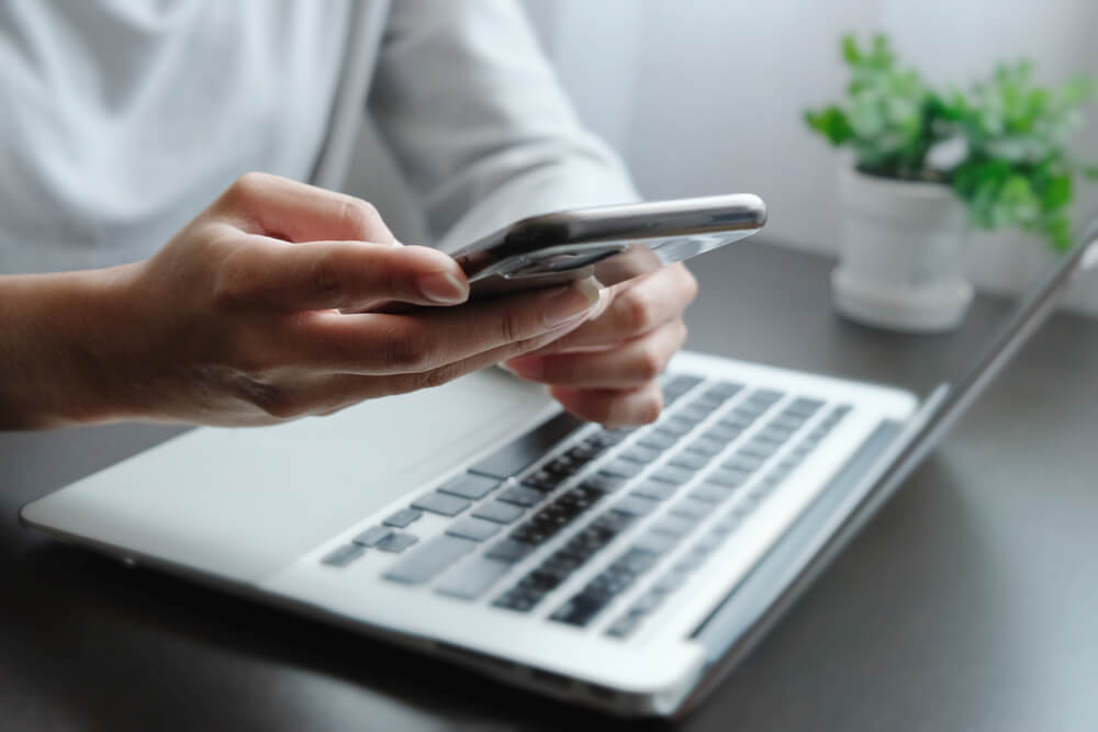 Blurred of Hand of Woman Using Smartphone in Front of Lap Top