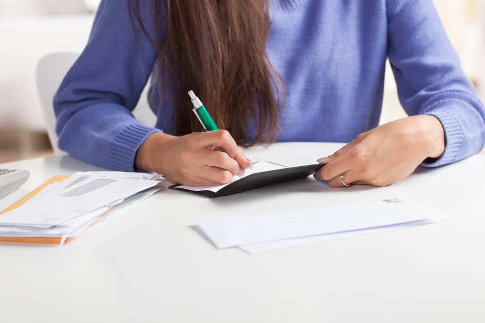 Attractive Young Hispanic Woman Sitting at Table Paying Bills and Doing Banking Wearing Blue Sweater.