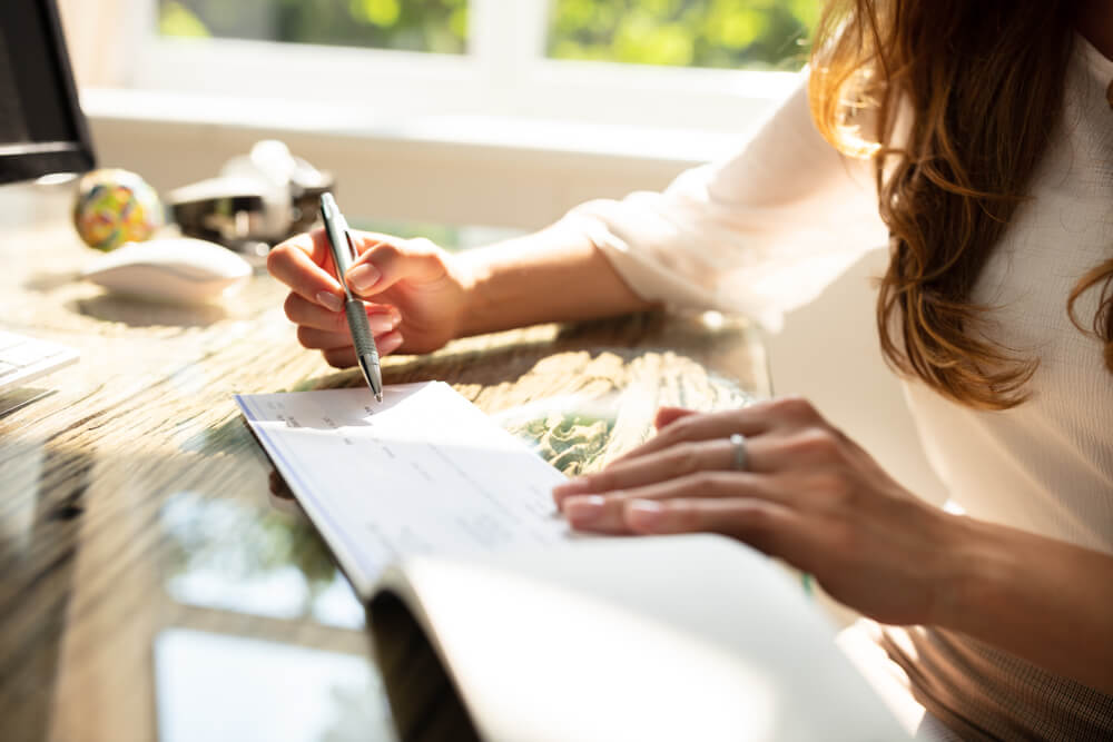 Businesswoman’s Hand Signing Cheque on Wooden Desk